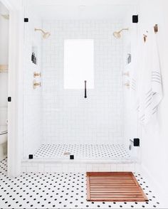 a white tiled bathroom with black and white floor tiles, gold fixtures and wooden bench