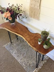 two vases with flowers are sitting on a wooden table next to a rug and wall hanging