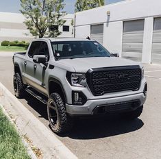 a silver truck parked in a parking lot next to a building with garage doors open