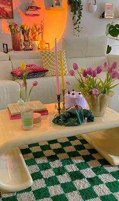 a table with flowers and candles on it in front of a white couch next to a green checkered rug