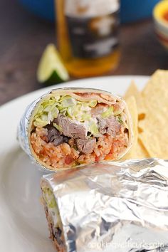 a burrito wrapped in aluminum foil on top of a white plate with tortilla chips