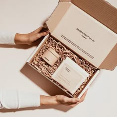 two hands are holding an open box with the contents inside it on a white surface