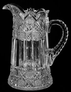 a clear glass pitcher with an ornate design on the front and sides, set against a black background