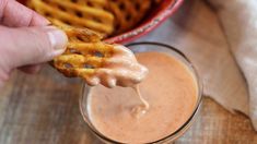 a hand holding a pretzel over a glass of milk