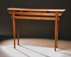 a wooden table sitting on top of a white floor next to a gray wall with light coming through it