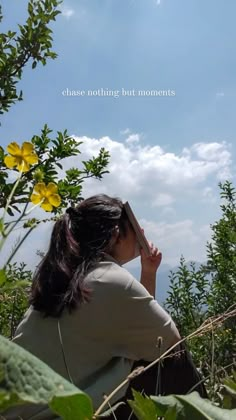 a woman sitting on top of a lush green field under a blue cloud filled sky