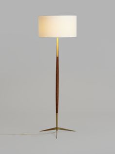 a floor lamp with a wooden base and a white shade on the top, standing in front of a gray background