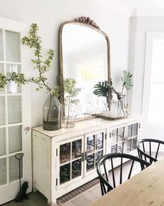 a dining room with a table, mirror and vases on top of the cabinet