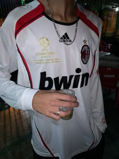 a man wearing a jersey holding a drink in his right hand and chain around his neck