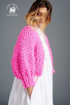 a woman wearing a pink knitted sweater and white dress with her hair blowing in the wind