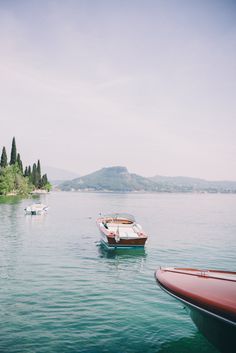 two boats floating on top of a large body of water next to a forest covered hillside