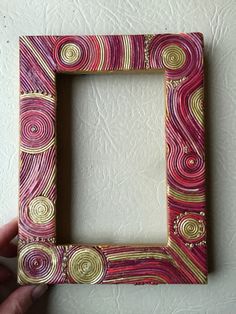 a hand holding up a pink and gold frame with swirls on the edges,