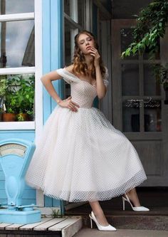 a woman in a white dress leaning against a blue door with her hand on her face