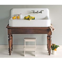 a white sink sitting on top of a wooden table next to a stool and potted plants