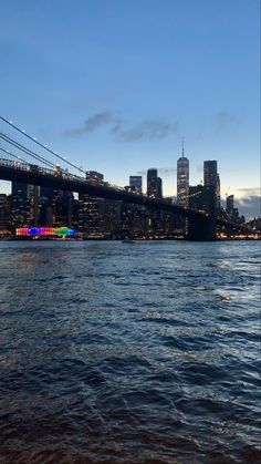 the city skyline is lit up at night as seen from across the water in front of a bridge