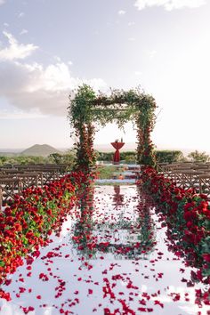 an outdoor ceremony setup with red flowers and greenery on the aisle, surrounded by rows of chairs