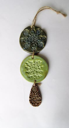 two ceramic ornaments hanging from a string on a white surface, one is green and the other is brown