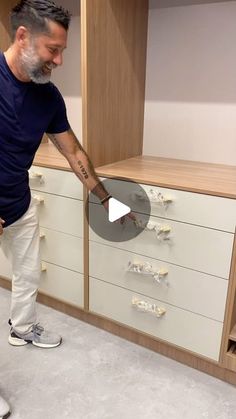 a man standing in front of a white cabinet with drawers on both sides and one arm extended