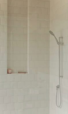 a white tiled shower with thermostaer and hand held shower head in it