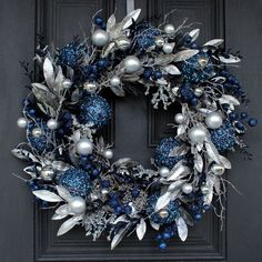 a wreath with silver and blue ornaments hanging on a black front door, surrounded by greenery