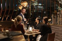 a group of people sitting around a table eating food and drinking wine in a restaurant