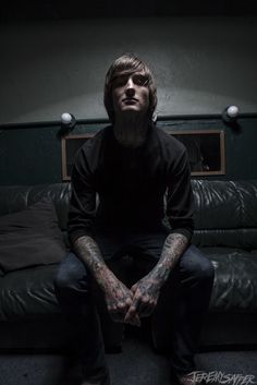 a man sitting on top of a couch next to a black leather sofa covered in tattoos