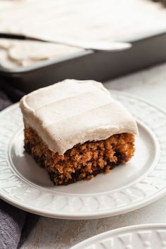 a piece of carrot cake with frosting on a plate next to a baking pan