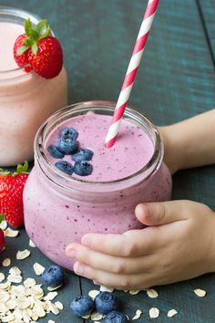 a person holding a straw in front of a jar of smoothie with blueberries and oats