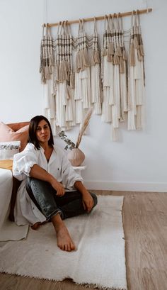 a woman sitting on the floor in front of a wall hanging with tassels