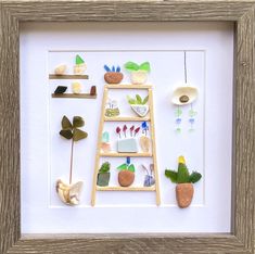 a wooden frame with some plants and rocks on the bottom, in front of a white wall