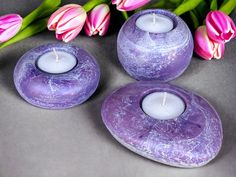 three purple candles sitting next to pink tulips on top of a gray surface