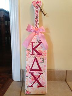 a decorated wine bottle with the word kaka on it and a pink ribbon tied to it