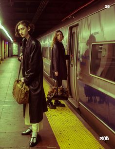 two people are standing on the platform next to a train and one is holding a bag