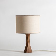 a wooden table lamp with a beige shade on it's side and a white background