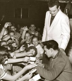 an old photo of a man signing autographs for young children in front of a crowd