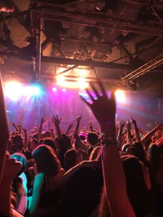 a large group of people at a concert with their hands in the air and lights on