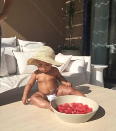 a small child sitting on the ground next to a bowl of strawberries