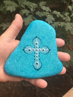 a hand holding a blue rock with a cross painted on it