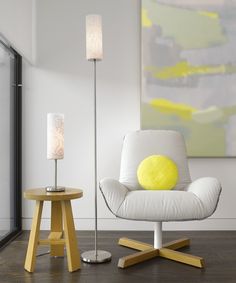 a white chair with a yellow pillow on it next to a wooden table and lamp