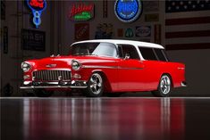 an old red and white station wagon parked in a garage with american flags on the wall