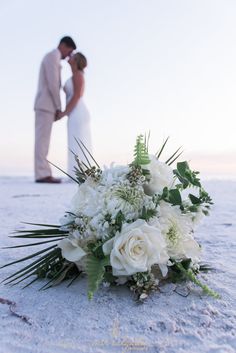 a bride and groom kissing on the beach with white flowers in front of their heads