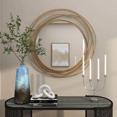 a black table with a blue vase and some white candles on it next to a round mirror