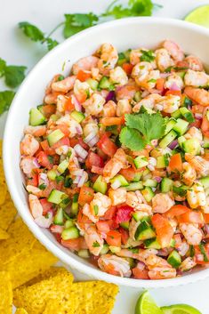 a white bowl filled with shrimp salad next to tortilla chips and cilantro