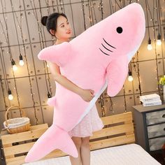 a woman holding a large pink shark pillow