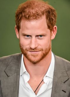 a close up of a person wearing a suit and smiling at the camera with a green background