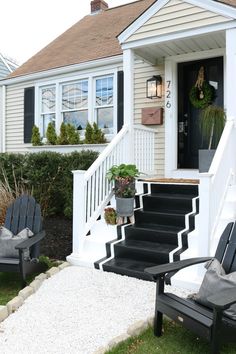 two lawn chairs sitting on the grass in front of a white house with black shutters