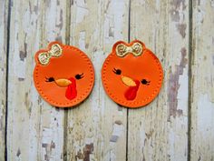 two orange patches with bows on them are sitting on a wooden surface, one has a turkey face and the other has a bow