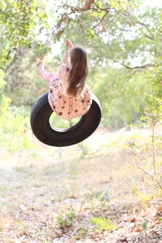 a girl swinging on a tire swing in the woods