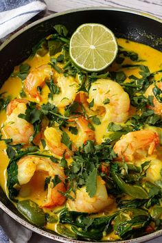 a skillet filled with shrimp and vegetables next to a slice of lime on the side