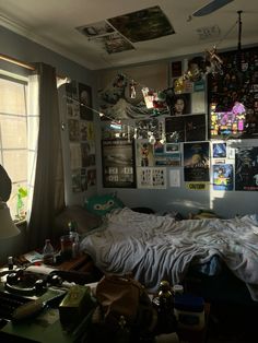 an unmade bed in a messy room with posters on the wall and windows above it